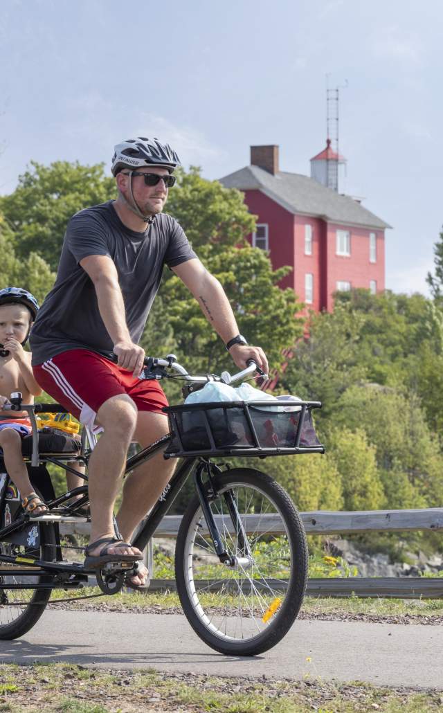 A father and his children biking near the Marquette Harbor Lighthouse, located in the Upper Peninsula of Michigan
