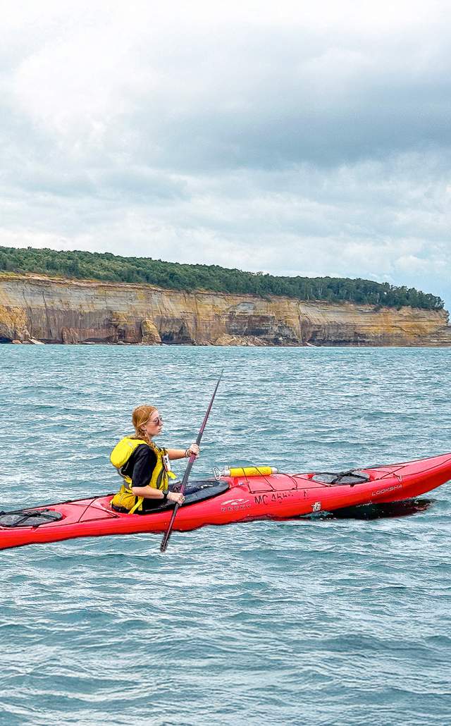 A woman kayaking along the shore of Pictured Rocks National Lakeshore
