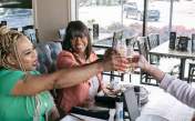 Three women raising their beverage glasses to cheers their meal at J.R. Neighbors