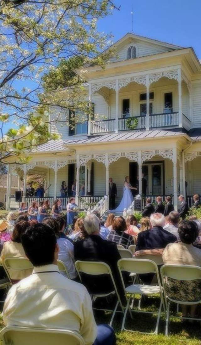 Outdoor wedding ceremony with guests seated on a lawn in front of the historic 1897 Poe House in Fayetteville, North Carolina.