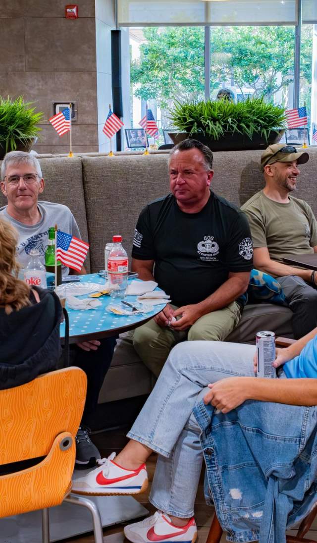Group of adults seated together at tables, talking and reconnecting during a casual reunion gathering in Greater Fayetteville.