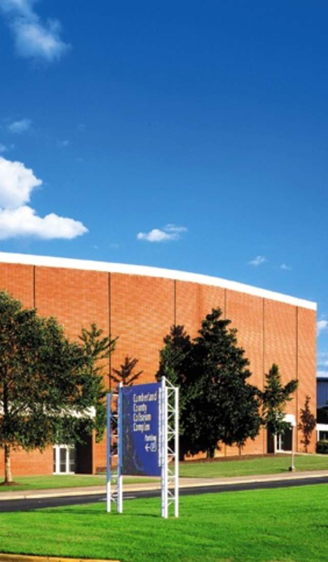 Crown Theatre exterior featuring a large brick facade, surrounding lawn, and clear blue sky in Fayetteville.