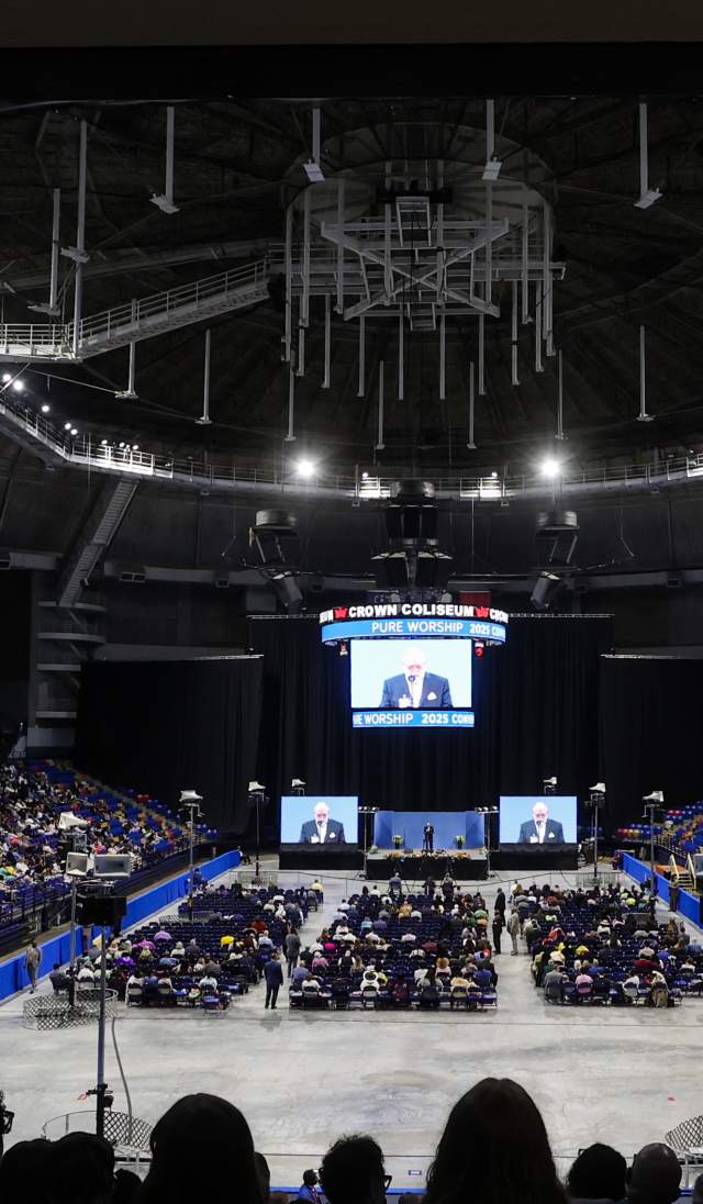 Wide view of attendees gathered inside Crown Coliseum in Fayetteville, NC for the Jehovah’s Witnesses Convention, with a speaker on stage and large screens visible to the audience