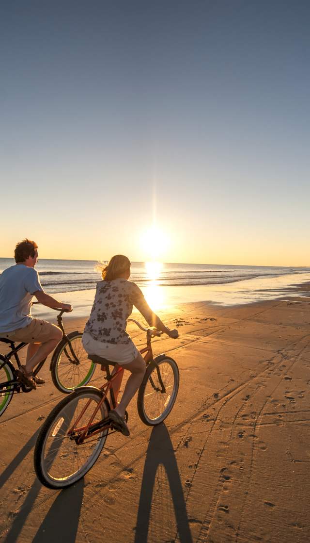 Couple riding bikes on wide beach at sunset