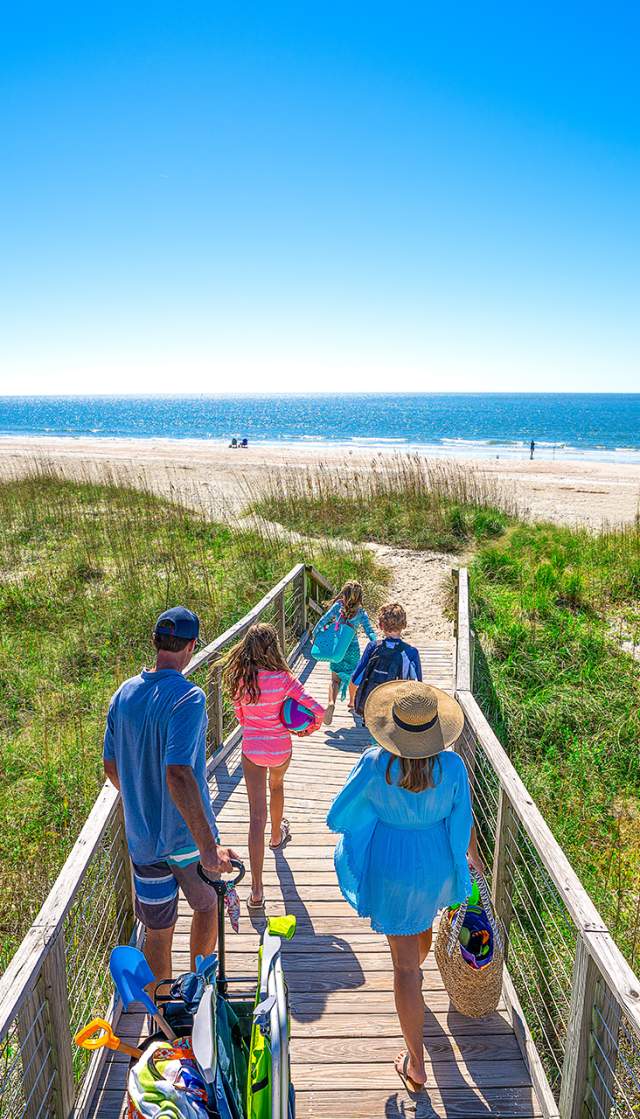 a family of 4 walking out to the beach on a wooden beach access