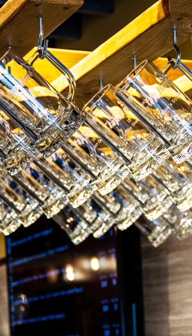 Rows of upside‑down beer glasses hanging from wooden racks inside a taproom interior in Brunswick County, North Carolina, with warm lighting and a bar area visible in the background.
