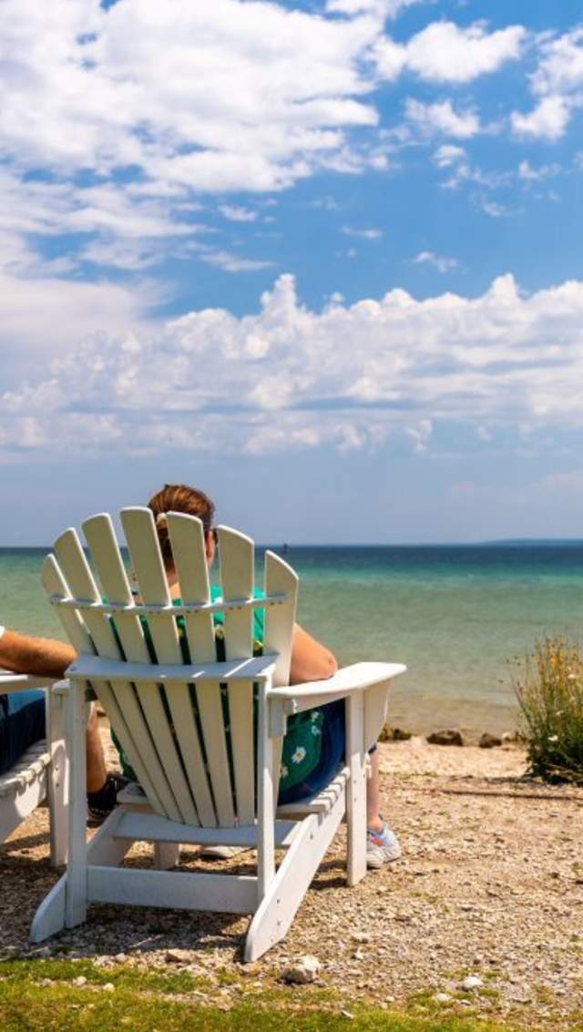 A couple relaxes on Adirondack chairs near the water on the beach at Mackinac Island’s Mission Point Resort