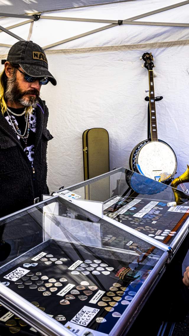 A man shows handmade guitars and accessories to a young shopper in his booth at the Covington Three Rivers Art Festival.