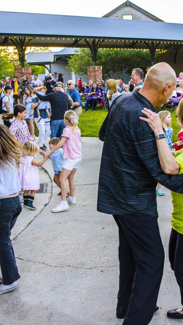 People of all ages dance near the stage during a Mandeville Live! free Friday concert at the Mandeville Trailhead, with a crowd gathered under the pavilion and on the lawn.