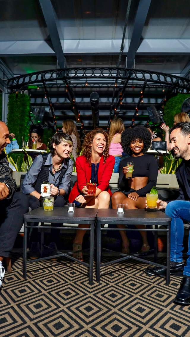 Group of five diverse friends socializing and enjoying colorful drinks at the stylish Rooftop @1WLO lounge with modern decor.