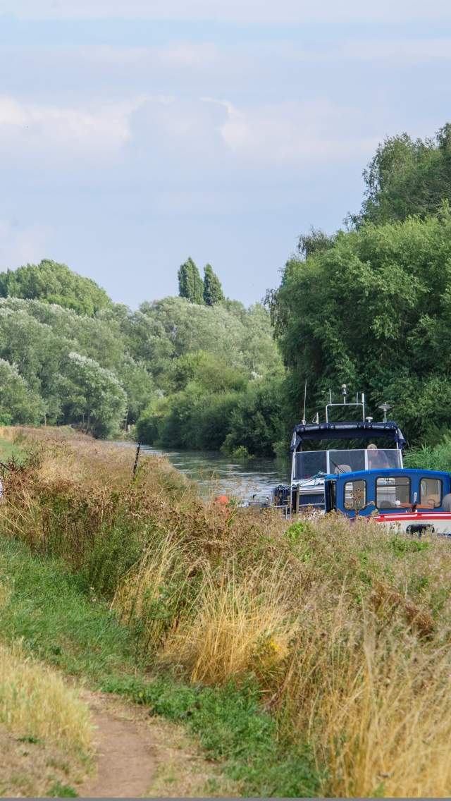 A cycle path running alongside the Fossdyke Canal, with people enjoying some alfresco dining in the distance.