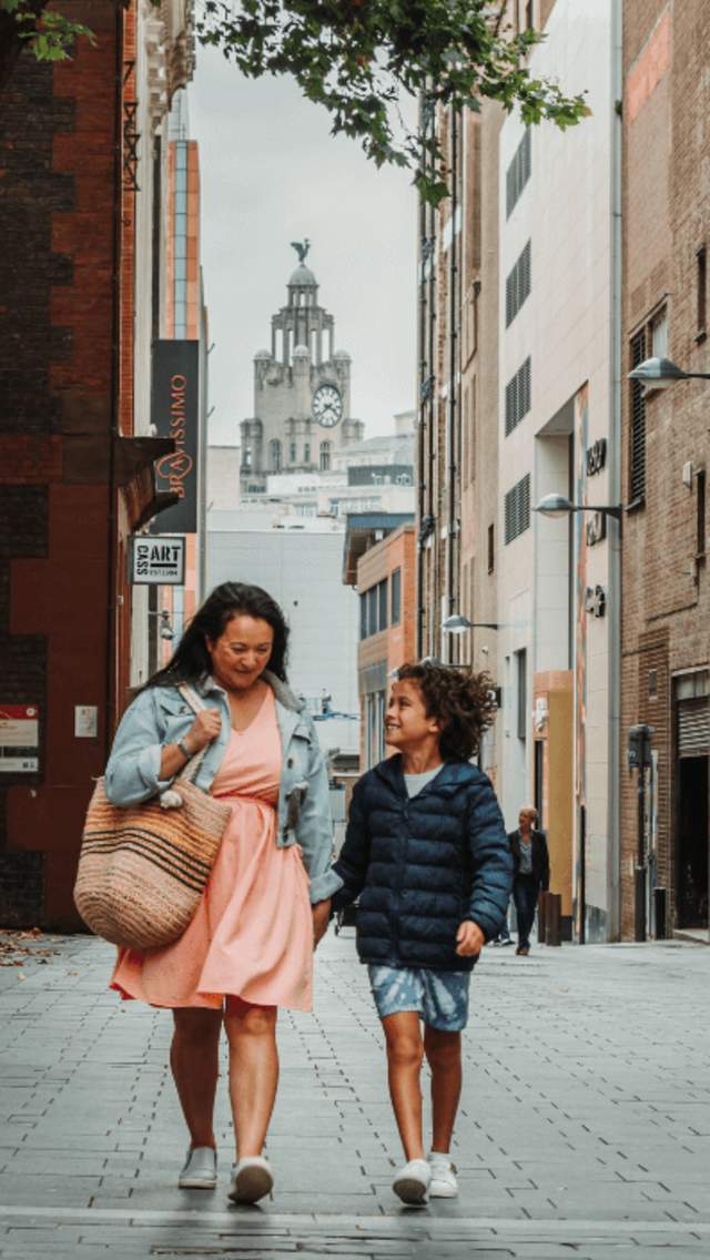 People are walking down a street in Liverpool city centre. They are laughing together and the Royal Liver Building is framed in the background of the shot