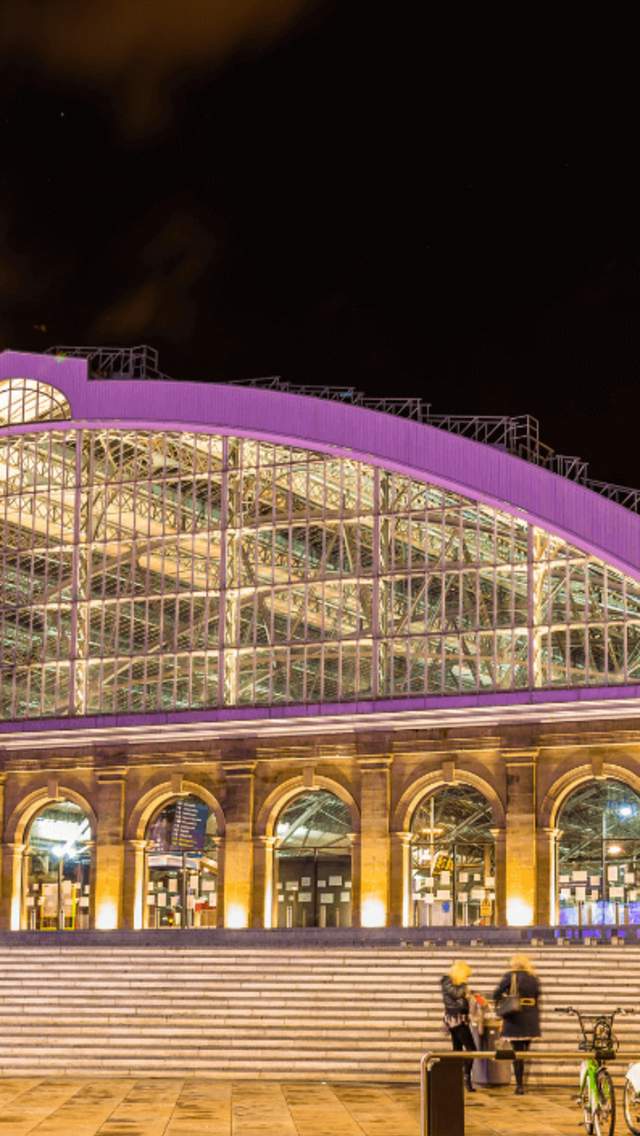 Exterior shot of Liverpool Lime Street Station at night. A large domed building with a glass archway and stone doorways below.