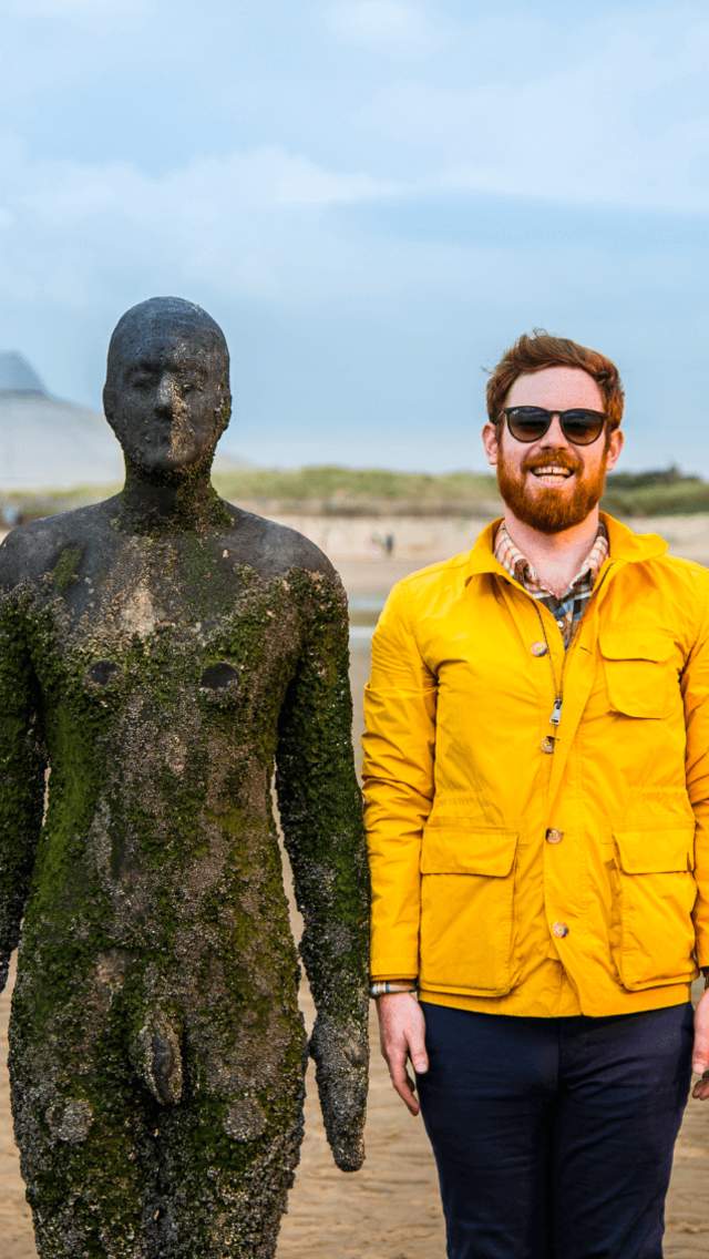 A man wearing a yellow raincoat stands next to a cast-iron statue