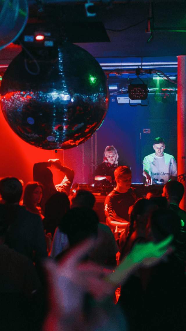 Inside a club with red lighting and a big disco ball