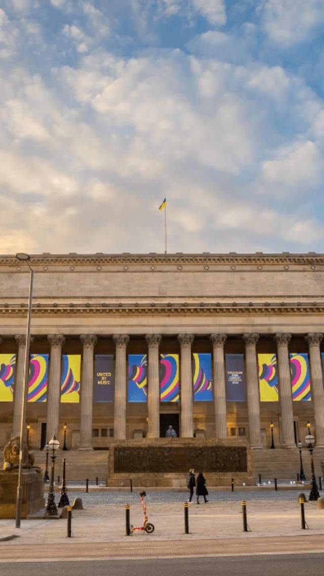 St George's Hall exterior with Eurovision banners, a blue sky and the sun setting to the left