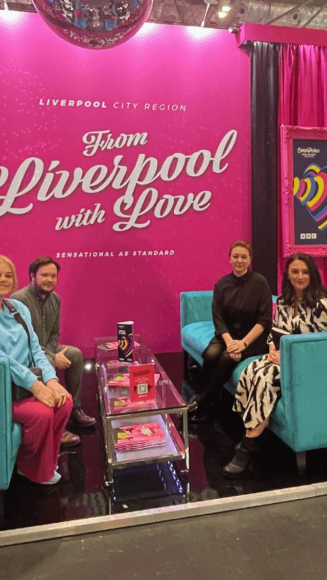 A large, bright pink exhibition stand with turquoise coloured couches. The team are wearimg