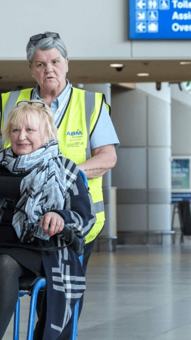 A member of staff pushes a lady in a wheelchair inside Liverpool Airport