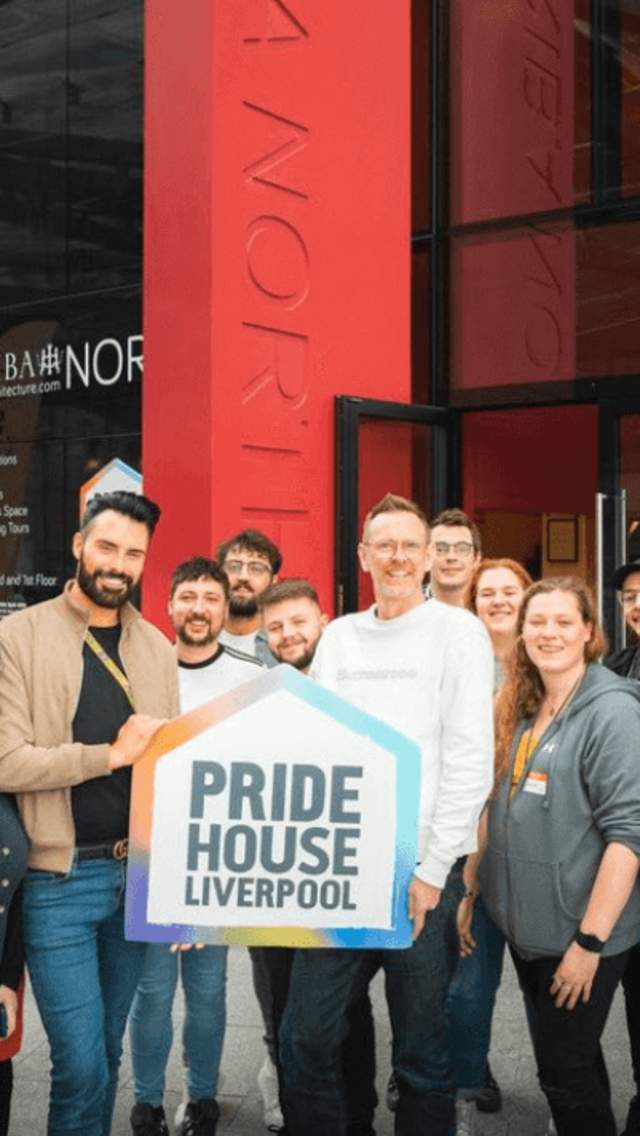 People stand outside Pride House holding the official Pride House sign
