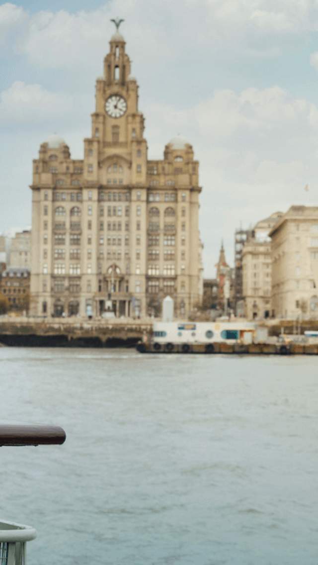 A young girl stands at the front of the Mersey Ferry on the river. In the background is the Liverpool skyline