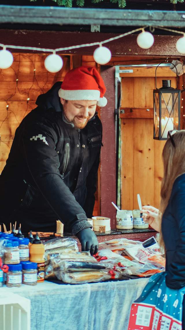 Mann som selger diverse delikatesser fra bod under julemarkedet i Sarpsborg. Foto.