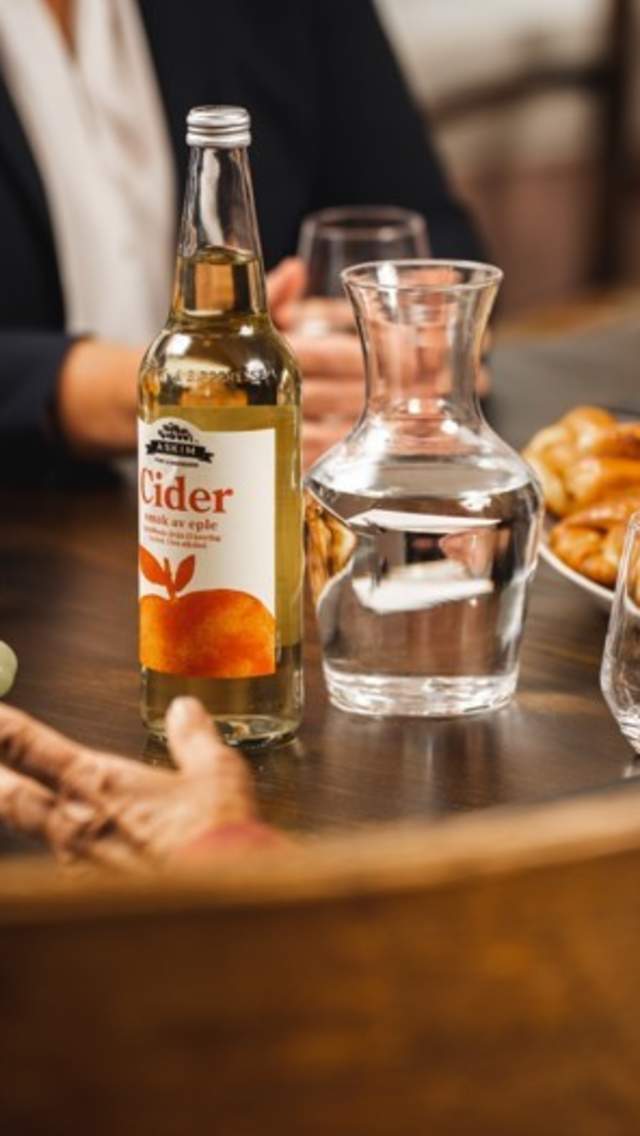 Bord med flaske fra Askim frukt og bærpresseri, frukt og folk som sitter rundt i møte