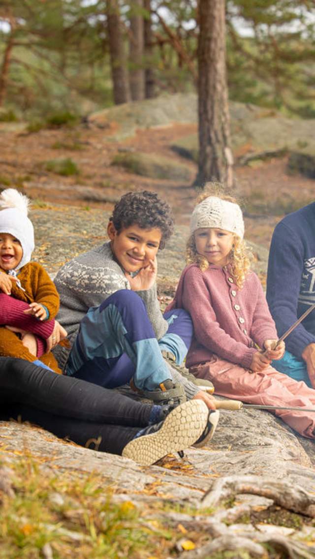 En familie på seks som sitter rundt bålet og griller pølser. Foto.