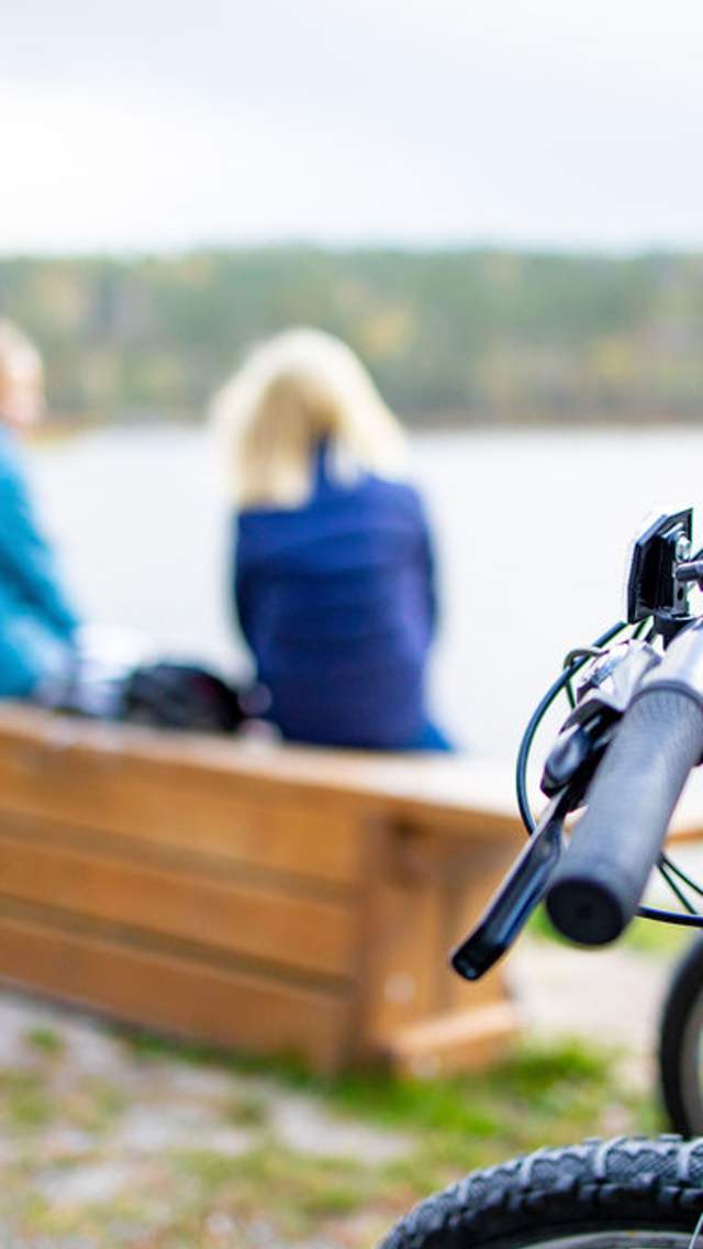 To jenter sitter på en krakk og ser ut mot havet. Syklene deres står i forgrunnen, og er i fokus.