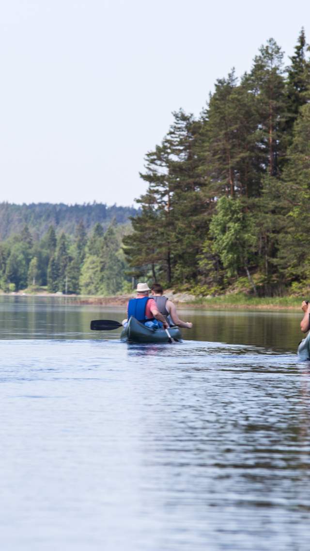 En gruppe mennesker fordelt i tre kanoer padler i sjøen.