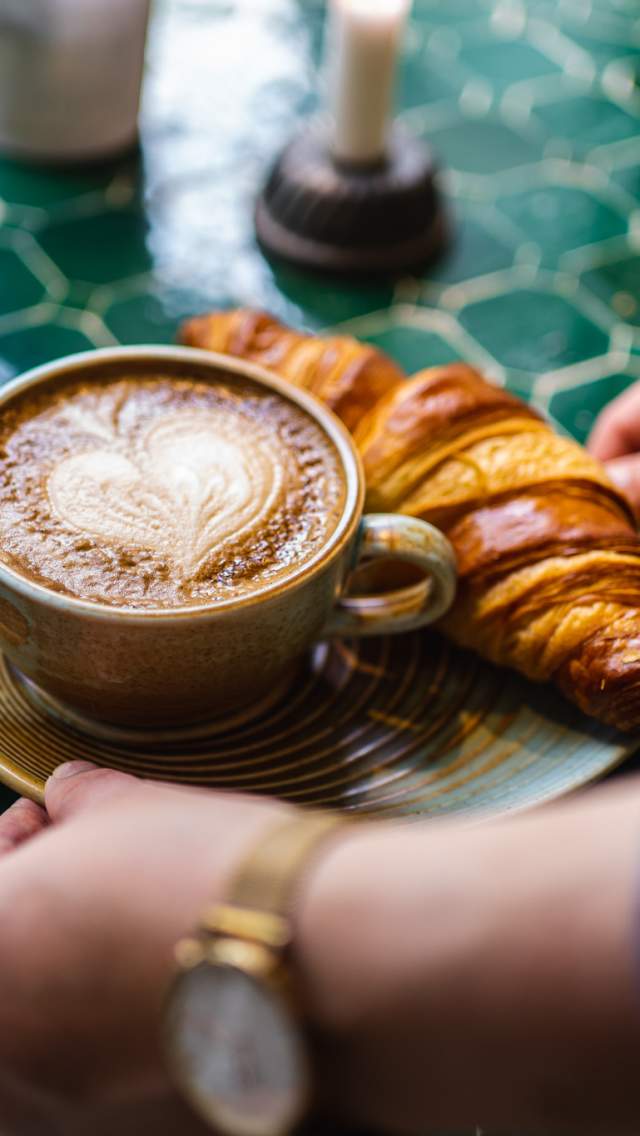 Kaffekopp med hjerteskum og en croissant servert på ett bord