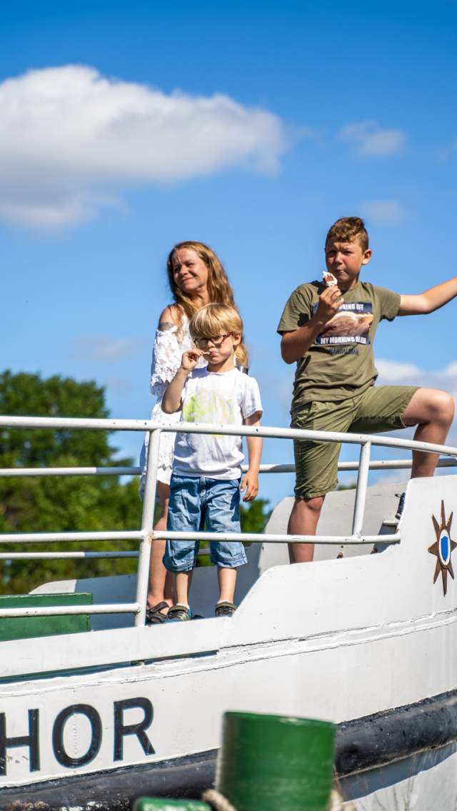 En dame og to barn står i baugen av båten Thor