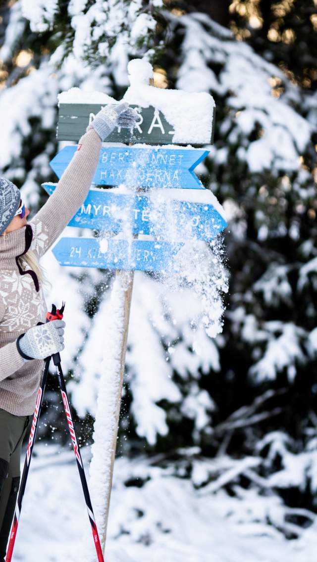 En dame børster av snøen på skiløypeskilt