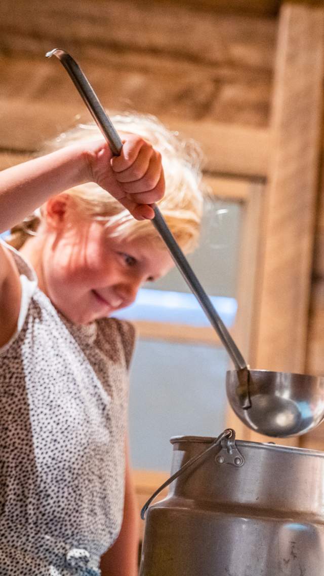 Jente som står og øser noe ut av grytene