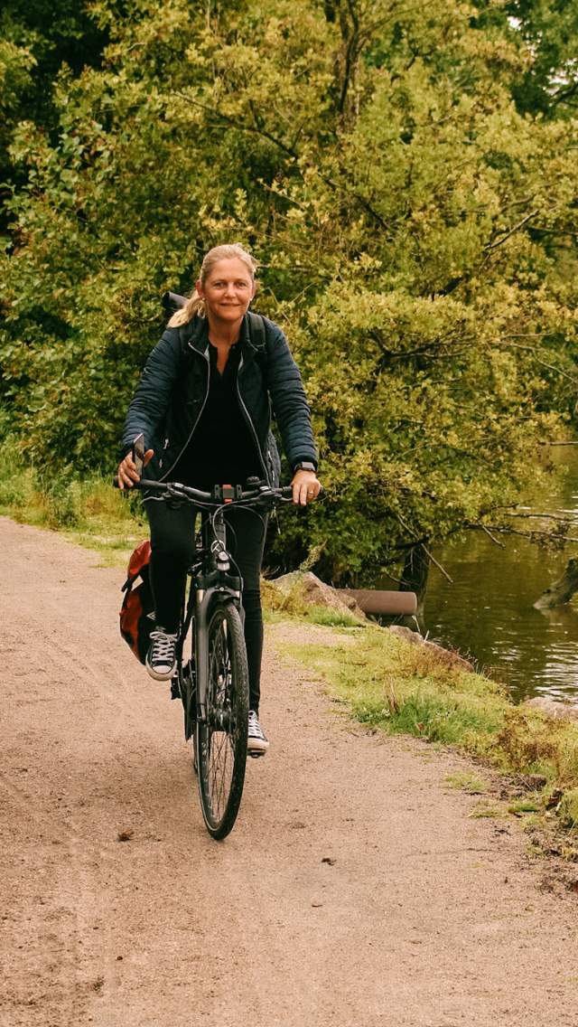 Kvinne som sykler langs en gruslagt vei på Glommastien, med Glomma i bakgrunnen.