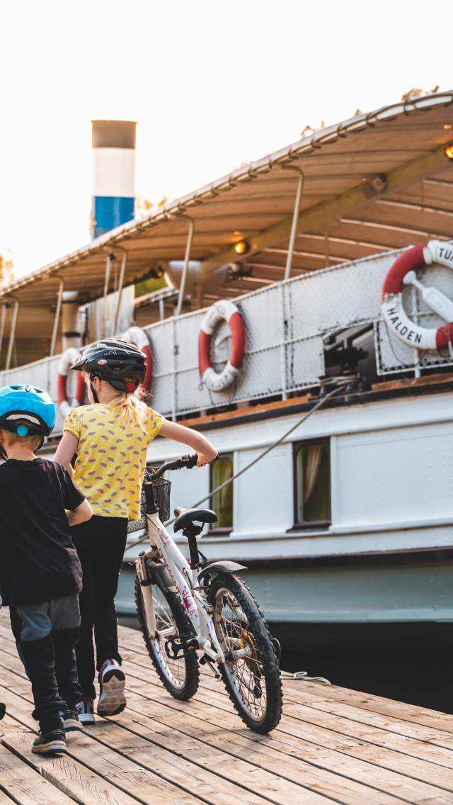 To barn som triller sykkelen ved siden av båten Turisten