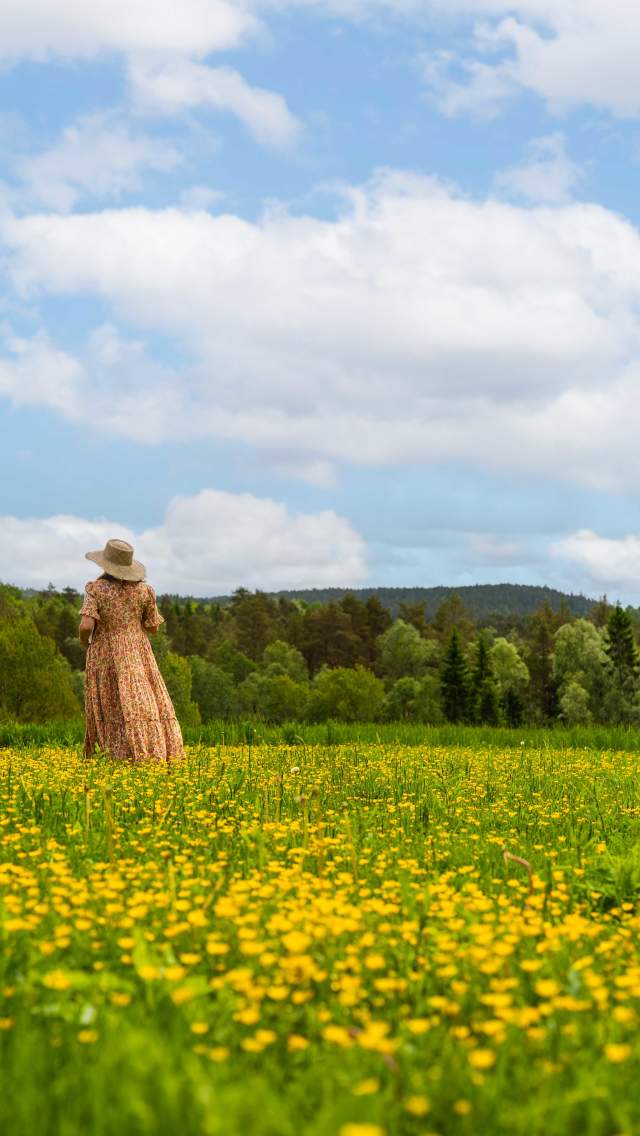 Kvinne i kjole som står i en blomstrende sommereng.