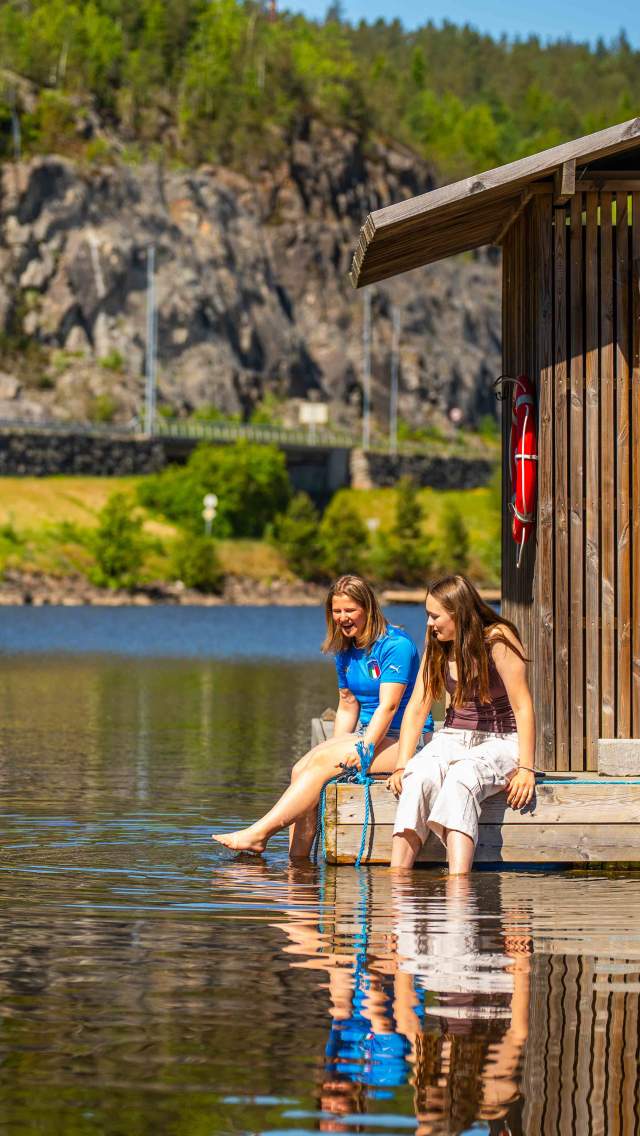 To jenter som dupper tærne i vannet på en brygge.