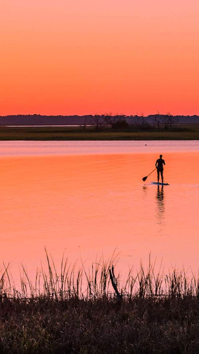 A group paddleboards through the calm marsh rivers at sunset in Golden Isles, Georgia