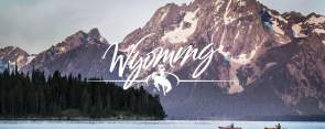 Persons kayaking on a serene lake with mountains and trees in the background in Wyoming.