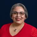 a portrait of a woman in glasses with a red shirt and gold necklace.