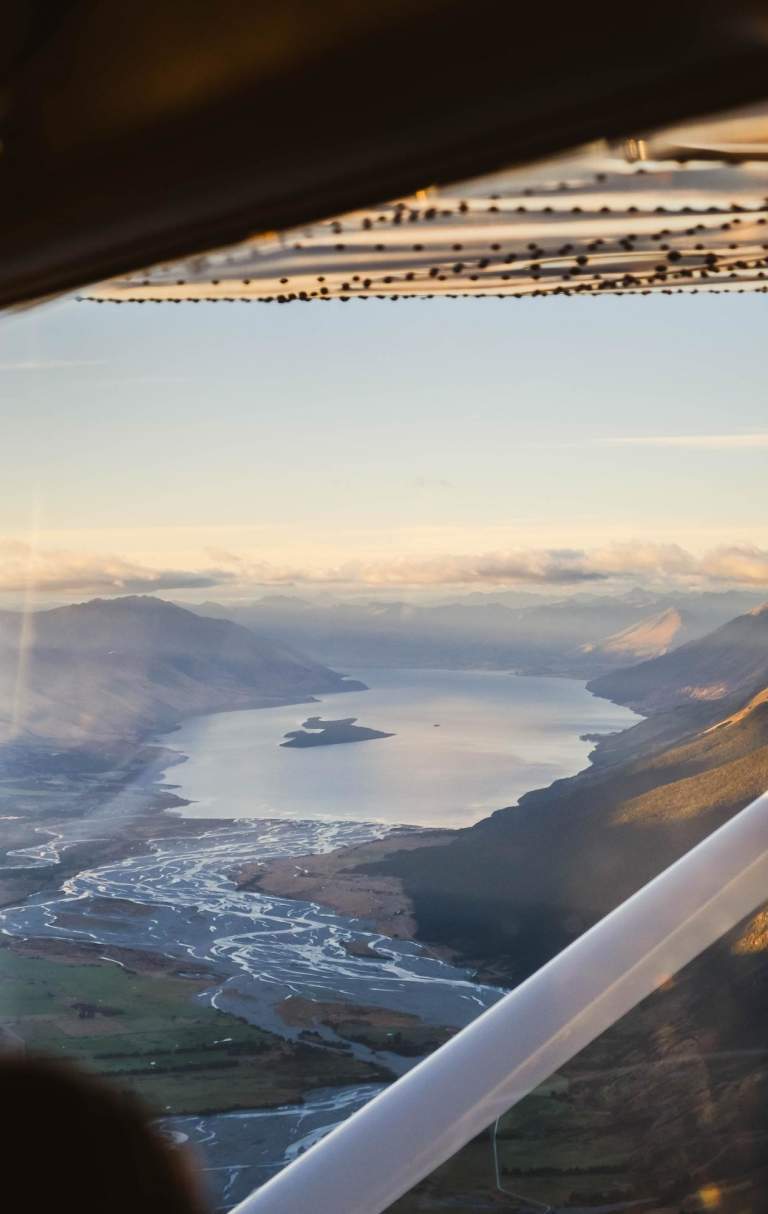 View from a plane window at sunrise looking out rivers, lakes and mountain ranges