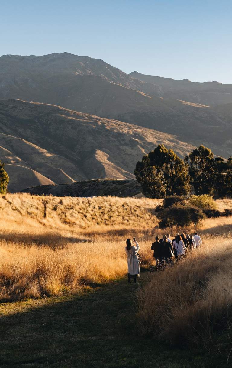 A group of people walking through a field with big autumn coloured mountains in the background