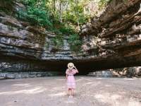 woman stands in dress and hat looking at cave entrance