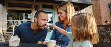 A young daughter feeding ice cream to her dad while her mom watches on the front patio of  Johnson's Ice Cream