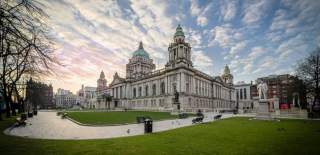 Photo of Belfast City Hall from outside looking at the grass areas and benches.