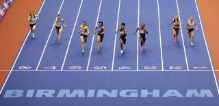 Eight runners race towards the camera on a blue running track with the Word BIRMINGHAM in bold letters at the end