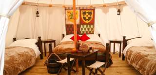 A glamping bedroom at Warwick Castle featuring three bed with fur throws, a small dining table with two chairs and two bed side tables