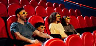 A man, his wife, and children sit in cinema seats wearing 3D glasses