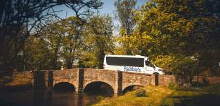A white mini bus with Rabbie's written on the side of it going over a bridge