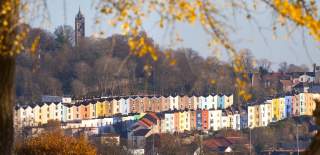 Rows of multi-coloured houses in the Cliftonwood area of West Bristol with autumn leaves in the foreground and Cabot Tower in the background